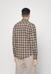 Chemise à carreaux avec un motif bleu, orange et blanc ; col boutonné ; manches longues ; tissu doux ; ourlet arrondi. Conception légère adaptée à l'empilement.