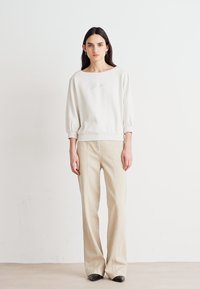 Lichtbeige sweatshirt met een wijde halslijn en driekwart mouwen, gecombineerd met off-white flare broeken. Zwarte, puntige schoenen zichtbaar.