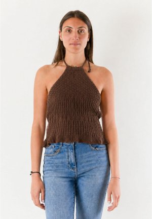 Donna in piedi di fronte, indossa un top marrone lavorato a maglia e jeans azzurri a vita alta su sfondo bianco.