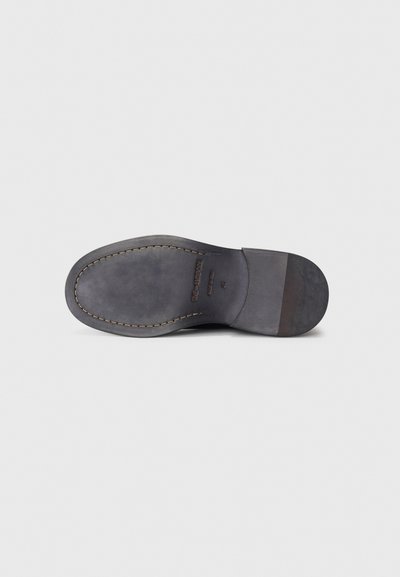 Semelle d'une chaussure habillée en cuir noir avec des coutures visibles, une finition lisse, et un texte en relief incluant "THE SANDROPE" et la taille 44.
