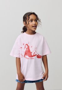 Tricou roz deschis supradimensionat din bumbac, cu un imprimeu grafic roșu reprezentând o fată cu stele și textul „I've always been” dedesubt.