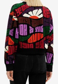 Sort sweatshirt med farverig grafisk skrift og blomsterdesign. Har ribstrikkede ærmeafslutninger og kant. Blødt, tekstureret stof.