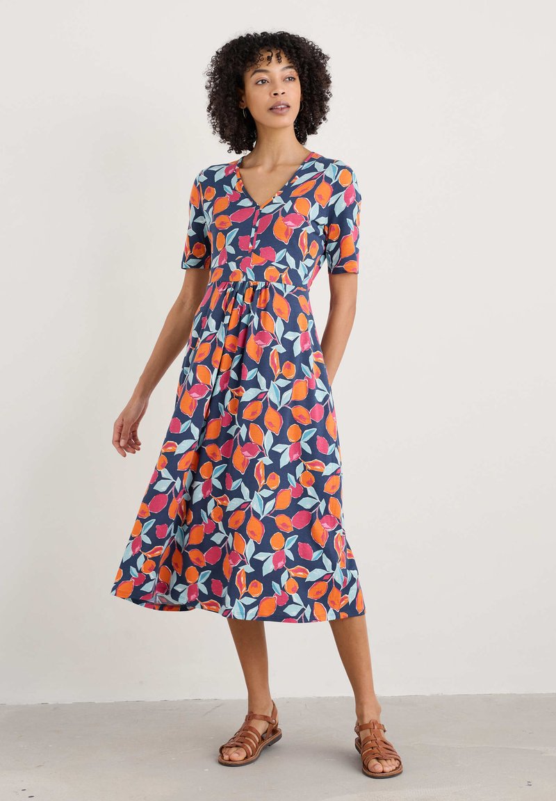 Floral dress with short sleeves, v-neck, featuring a navy background and vibrant orange, pink, and teal leaf patterns. Mid-length design.