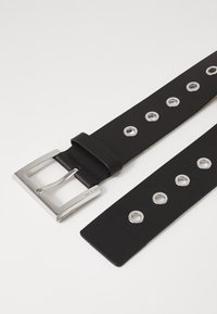 Czarny skórzany pasek z prostokątną srebrną klamrą i wieloma srebrnymi oczkami na białym tle.