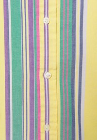 Camisa abotonada a rayas con base amarilla y líneas en verde, púrpura, rosa y gris. Tejido suave con textura lisa.