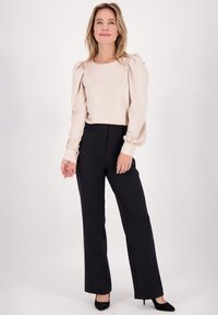 Beige blouse met opgestoken mouwen, gecombineerd met hoge zwarte broek en zwarte hakken; gladde stof en op maat gemaakte uitstraling.