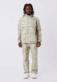 Lichtgroene, gestructureerde hoodie met een voorzak, gecombineerd met bijpassende cargobroek met zijzakken. Witte sneakers maken de outfit compleet.