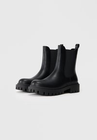 Botas negras hasta el tobillo con un acabado en cuero suave, paneles elásticos a los lados y suelas de goma gruesa con un diseño de dibujo.