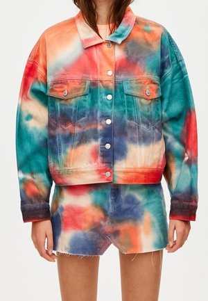 Femme portant une veste en jean tie-dye colorée avec fermeture à boutons et une jupe en jean assortie à ourlet effiloché.