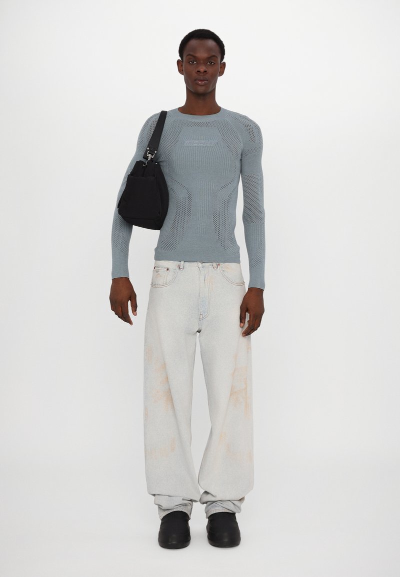 Lichtblauw gebreid longsleeve top met netdetails, gecombineerd met wijde vervaagde jeans. Een zwarte crossbodytas hangt over één schouder.