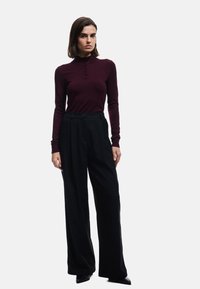 Bordeaux longsleeve top met hoge kraag en knoopdetails, gecombineerd met losse zwarte broeken, met een zachte textuur en een op maat gemaakte pasvorm.