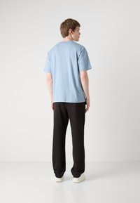 Lyseblå t-skjorte med korte ermer og rund hals, kombinert med sorte bukser og hvite sneakers. Stoffet virker jevnt og uformelt.