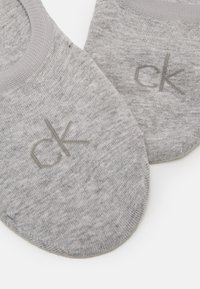 Sive pamučne čarape do gležnja glatke teksture, s diskretnim "ck" logotipom u malo tamnijoj sivoj boji. Dizajn s okruglim rubom.