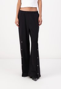 Pantalones de pierna ancha negros con una cintura elástica, con botones a presión dorados a lo largo de las costuras laterales. Hechos de una tela ligera y suave.