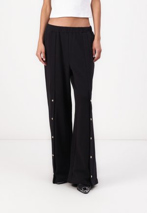 Pantalons larges noirs avec une taille élastique, ornés de boutons-pression en or le long des coutures latérales. Fabriqués dans un tissu lisse et léger.