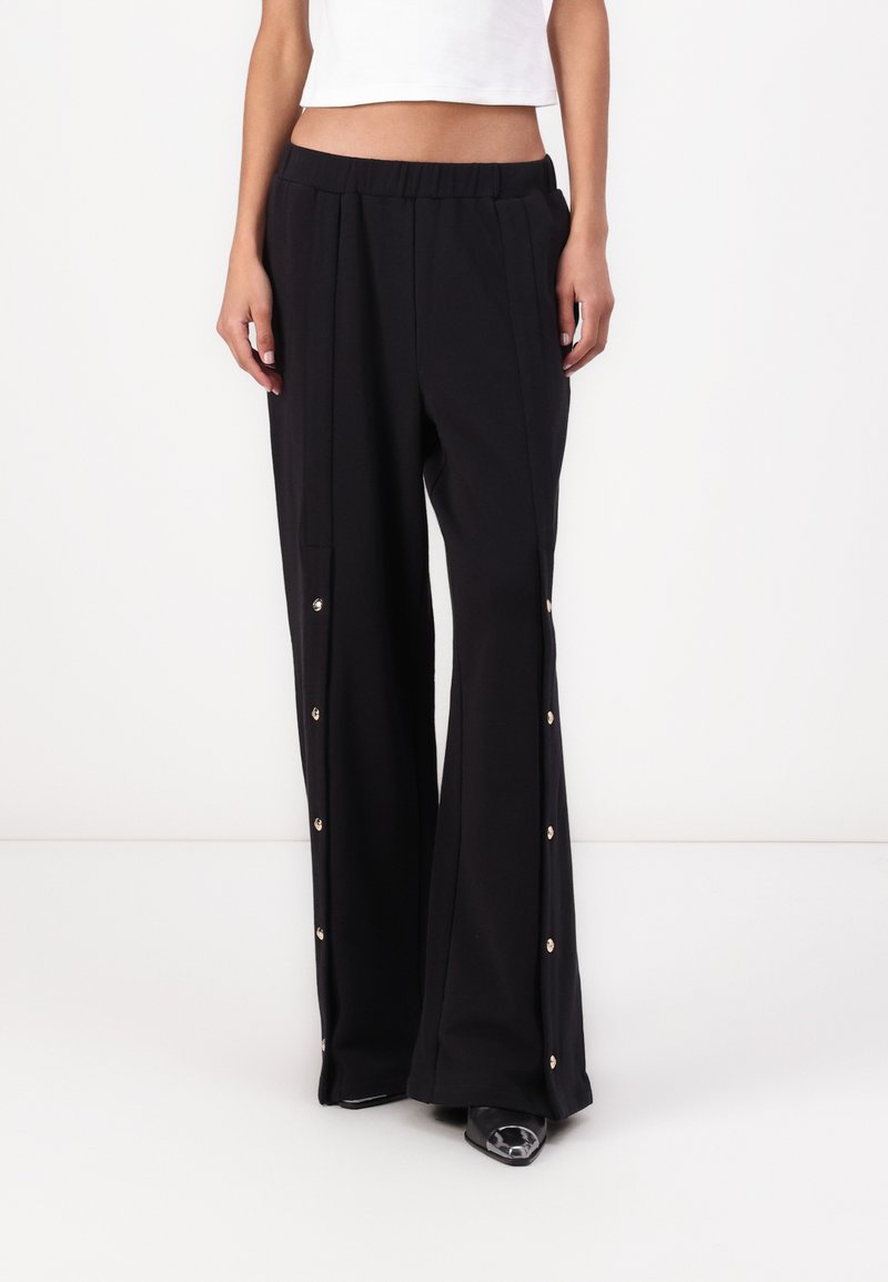 Pantalones de pierna ancha negros con una cintura elástica, con botones a presión dorados a lo largo de las costuras laterales. Hechos de una tela ligera y suave.