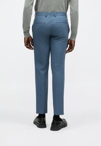 Világoskék, szabott nadrág sima textúrával, karcsúsított fazonban, övbújtatókkal. Két hátsó zsebbel és fekete, egyszínű cipővel zoknival.