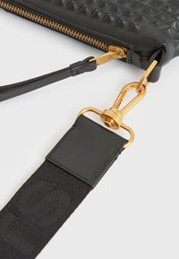 Sort clutch-taske med en struktureret diamantmønster, guld lynlås og hardware, samt en aftagelig sort stofrem.