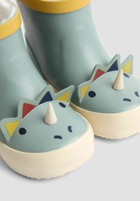 Gumené čižmy v bledomodrej farbe so žltými detailmi. Obsahujú dizajn s tvárou dinosaura so stredným ostňom a farebnými akcentmi (červená, modrá, žltá).