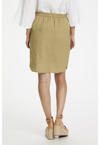 Jupe vert olive clair avec une taille élastique, longueur au genou, avec des fentes latérales pour faciliter le mouvement. Associée à des sandales compensées couleur marron clair.