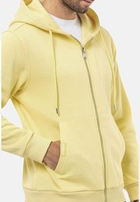 Geel zip-up hoodie van zachte stof, met een voorzak, trekkoorden en geribde manchetten. Minimalistisch ontwerp met logo-accent.