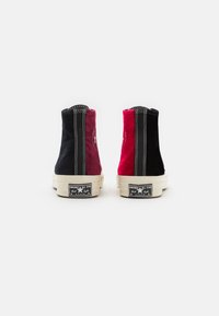 Sneaker alte con un design a spicchi in suede nero e rosso scuro, cuciture bianche a contrasto e suole in gomma con dettagli del logo.