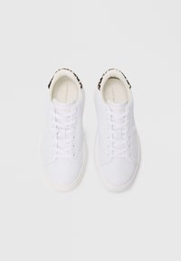 Adidași albi cu un superior din piele netedă, vârf rotund, șireturi plate și un guler texturat cu un model negru și bej. Branding subtil pe lateral.