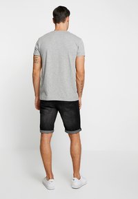 Maglietta di cotone grigia con maniche corte, abbinata a pantaloni corti di jeans neri con orlo arrotolato e sneakers bianche, vista da dietro.