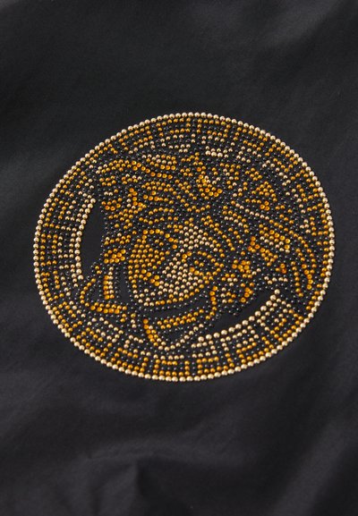 Svart tyg med ett cirkulärt mönster av guld-, svart- och orangea rhinestones, som visar en detaljerad design med intrikata dekorationer.