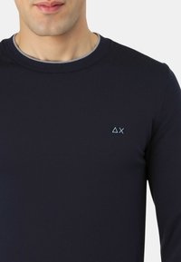 Marineblaue langärmelige Hemd aus glattem Stoff, mit einem runden Kragen und einem kleinen, hellblauen Logo auf der linken Brust.