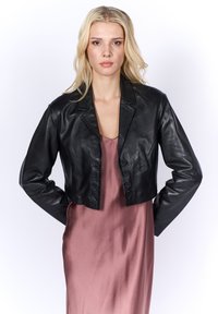 Giacca in pelle nera tagliata con colletto a punte, chiusura frontale con bottoni e maniche lunghe, indossata sopra un vestito di seta rosa.