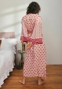 Ilga, raštuota rožinė chalatą su raudonu gėlių ornamentu. Turi plačius rankovės, dekoruotus raudonais zigzago akcentais, ir atitinkamą diržą juosmens srityje.