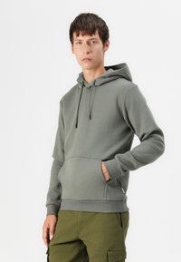 Hooded sweatshirt in olive green, featuring a kangaroo pocket, drawstrings, and ribbed cuffs. Made from soft, textured fabric.
