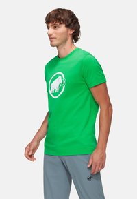 Camiseta de algodón verde con un gráfico blanco de un mamut dentro de un diseño circular. Mangas cortas, escote redondo, ajuste Slim.