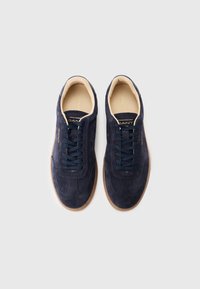 Baskets en suède bleu marine avec design à lacets, doublure crème et semelle en caoutchouc marron clair. Logo embossé sur le côté.