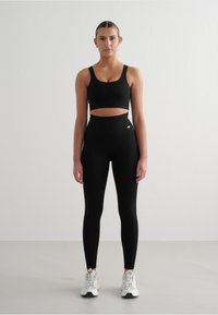 Schwarzes geripptes Sport-BH- und high-waisted Leggings-Set, das ein verkürztes Design und eine glatte Textur aufweist. Weiße Sneaker mit Schnürsenkeln vervollständigen den Look.