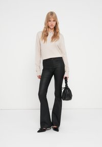 Pantaloni neri a zampa d'elefante abbinati a una maglietta a maniche lunghe beige chiaro, con una borsa nera strutturata. Tessuto morbido, silhouette rilassata.