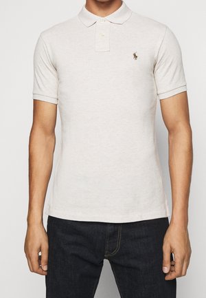 Crème polo shirt van gestructureerd katoen, met een drie-knoop sluiting en een klein geborduurd logo op de linkerborst. Gecombineerd met donkere jeans.