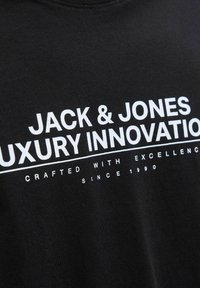 Svart bomull T-shirt med fet vit text som säger "JACK & JONES LUXURY INNOVATION" och mindre text under.
