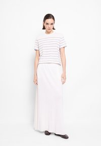 Lekki, prążkowany top dzianinowy w białym i szarym kolorze, połączony z długą, miękką, kremową spódnicą. Gładka tekstura; minimalistyczny design.