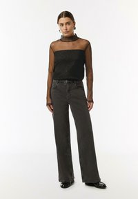 Schwarzes, transparenter Langarmoberteil mit glitzernden Akzenten, kombiniert mit hoch taillierten, geraden dunklen Jeans und schwarzen Lacklederschuhen.