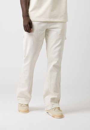 Beige cargobroek met een losse pasvorm, voorzien van voorzakken, gestikte details en een rechte pijpdesign. Draagt met lichtgekleurde sneakers.