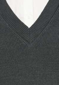 Maglione grigio lavorato a maglia con scollo a V, caratterizzato da una texture a coste e dettagli discreti. Il colletto rivela una camicia bianca sotto.