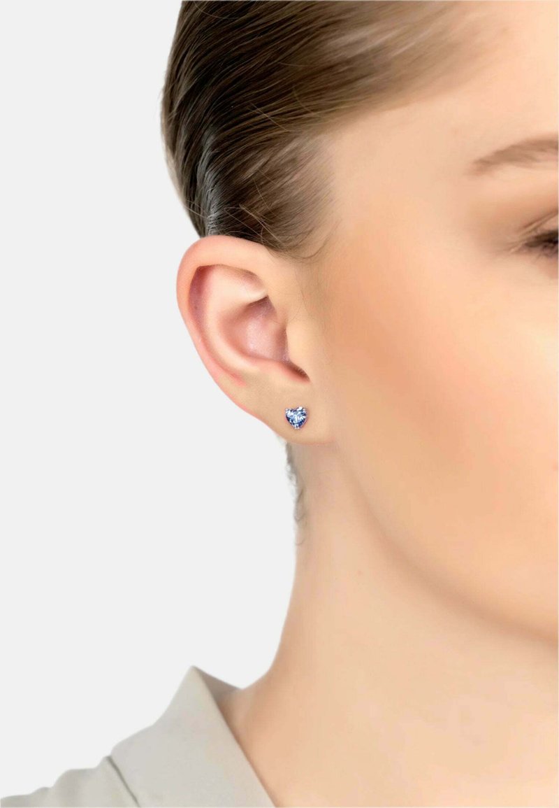 Hjärtformad studshering med en blå ädelsten inlagd i silver, visad på en models öra. Slät yta, liten storlek, elegant design.