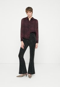 Blusa bordeaux con motivo, dalla vestibilità rilassata, abbinata a pantaloni neri svasati con un design ondulato in argento e mule grigio chiaro a punta.