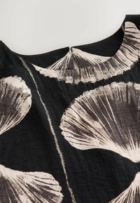 Tissu noir avec un grand motif floral blanc, présentant une surface texturée et un col rond avec une petite fermeture à bouton au dos.