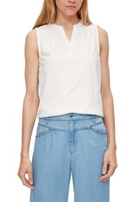 White sleeveless top with a notch collar, pleated shoulders, and soft texture, paired with light blue denim, featuring two hip pockets.