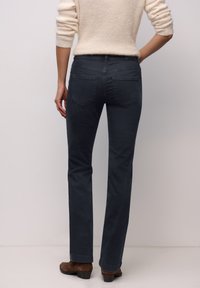 Jean gris foncé ajusté avec une coupe droite, poches arrière et texture lisse. Porté avec un pull crème et des chaussures marron.