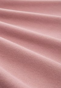 Tela de algodón rosa con una superficie texturizada y acanalada, mostrando múltiples pliegues y una apariencia suave y lisa. Distribución de color uniforme en toda la tela.