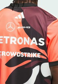 Maglietta a maniche corte arancione e nera con una finitura lucida. Presenta loghi stampati: PETRONAS, MERCEDES, AMG, e disegni di forme astratte.